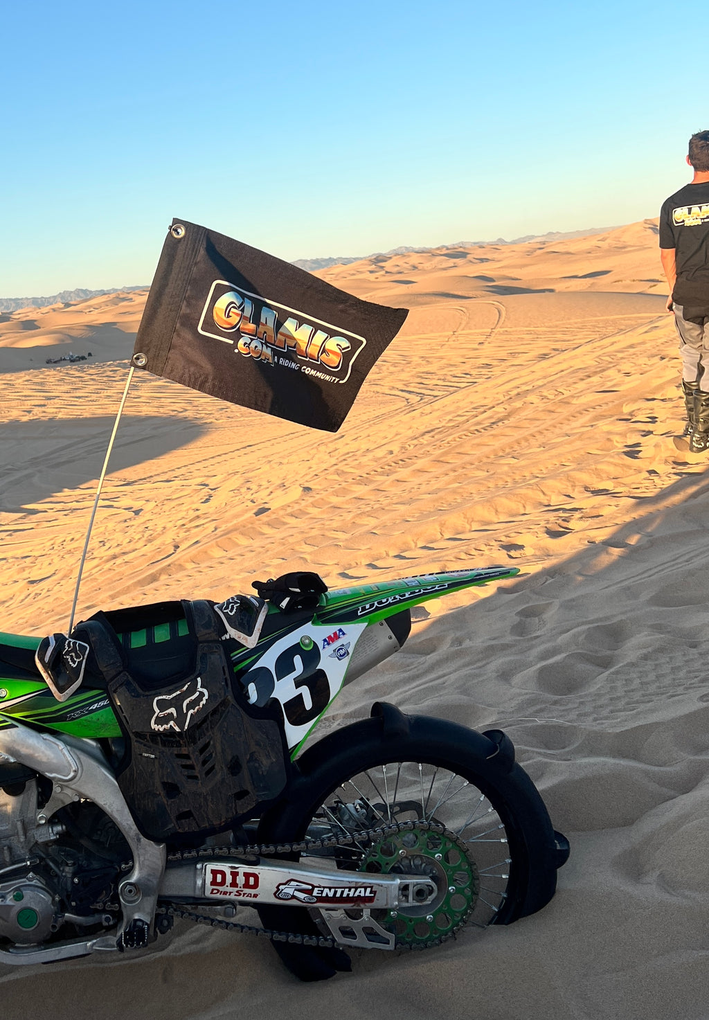 Glamis.com 12x18 inch whip flag with colorful design, fluttering in the wind, mounted on a pole against a clear sky.