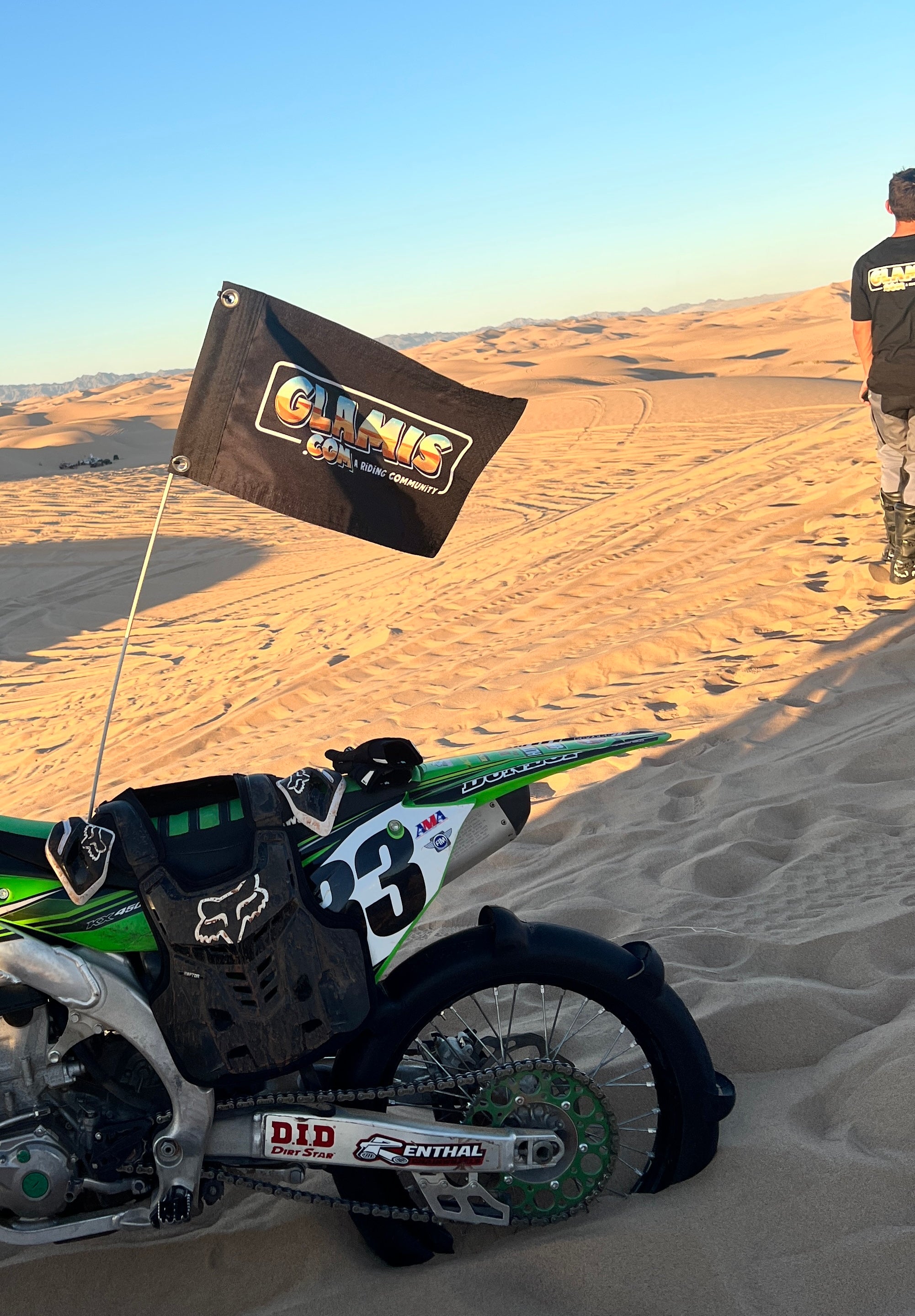 Glamis.com 12x18 inch whip flag with colorful design, fluttering in the wind, mounted on a pole against a clear sky.